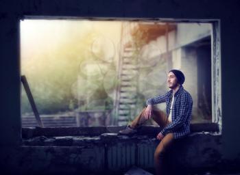 Stalker, male traveler sitting on the window, ruins of the abandoned city on background. Danger zone, post apocalypse horror