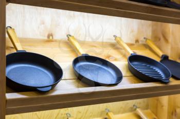 Frying pans on wooden shelf closeup, cooking tools. Kitchen decoration, iron utensil
