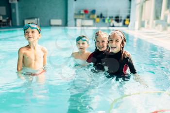Portrait of friendly children with swimming goggles in pool. Healthy and happy childhood concept. Funny children in swimming pool.Boys and girls in clean blue water.