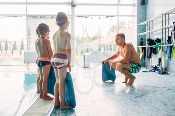 Instructor training children in the pool. Boys with swimming goggles ready for swimming and stands near water. Healthy activity in pool. Sportive kids activity in modern sport center with pool.