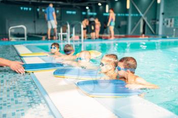 Instructor gives child plank for swimming. Children in water with goggles are going to do swim exercise. Healthy activity in pool. Sportive kids activity in modern sport center with pool.