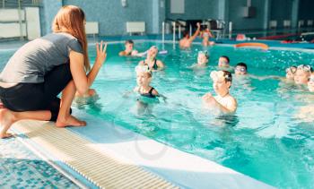 Woman instructor works with children in swimming pool. Kids with goggles in water listening female trainer. Happy kids in modern sport center. Concept of fun, leisure and recreation.