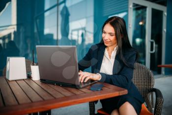 Business woman works on laptop in office. Modern building, financial center, cityscape. Female businessperson in suit at workplace