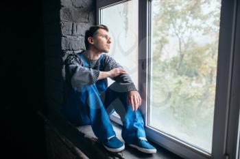 Depressed man sitting on the window sill in dark room, psycho patient. Mentally ill people concept, stressed human, depression