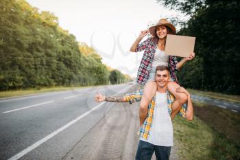 Young hitchhiking couple with empty cardboard. Hitchhike adventure of man and woman. Happy hitchhikers on road