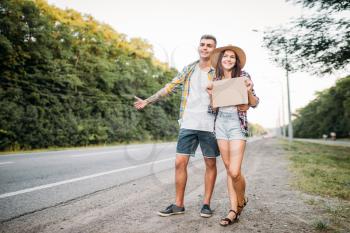 Young hitchhiking couple with empty cardboard. Hitchhike adventure of man and woman. Happy hitchhikers on road