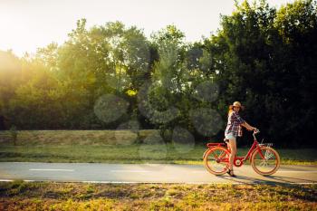 Young woman riding on red vintage bicycle in summer park on sunset. Cycling outdoor. Girl on retro cycle