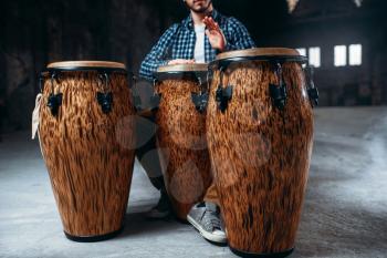 Male drummer plays on wooden drums in factory shop, musician in motion. Bongo, musical percussion instrument, ethnic music