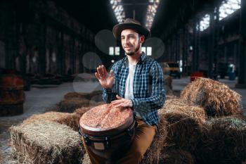 Young male drummer against african wooden drum, factory shop on background. Djembe, musical percussion instrument