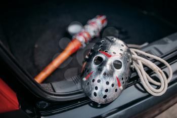 Hockey mask, baseball bat wrapped with bloody metal chain, duct tape and rope closeup, serial murderer concept. Psycho man instruments in opened car trunk, maniac. 