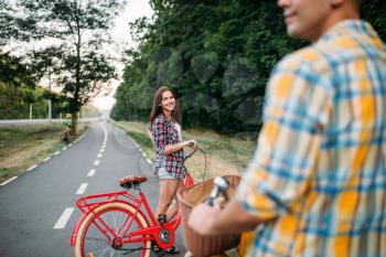 Male person and young woman riding on retro bikes. Couple on vintage bicycles. Young man and woman on old cycles, romantic date