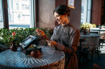 Young happy woman in cafe with casket and jewelry. Portrait of beautiful young retro lady with beads in her hands. Smiling brunette in vintage dress sitting in cafe.