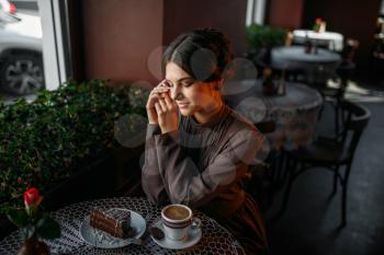 A young beautiful girl with a cup of coffee in retro style cafe. Smiling woman in cafe with dessert and cup of coffee. Chocolate cake on a white plate.