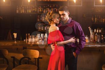 Beautiful woman in red dress hugs with her man in bar. Date in nightclub, attractive love couple in pub