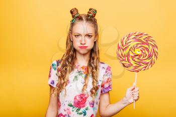 Sad teenage girl holdss big lollipop. Happy teenager with colorful caramel candy, yellow background in studio. Happy smiling girl with bright makeup.