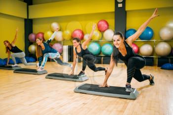 Athletic women in sportswear on step aerobic workout indoor. Female sport teamwork in gym. Fit class, fitness exercise in motion