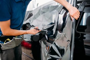 Male specialist with scissors, car tinting film installation process, tinted auto glass installing procedure