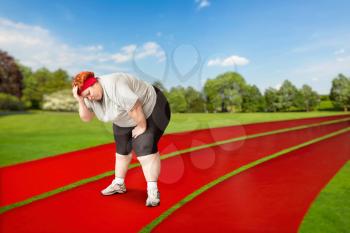 Overweight tired female runner on a jogging track outdoors. Calories burning, obese woman after running exercise