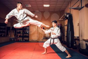 Martial arts karate masters in white uniform and black belts practice kick in jump. Taekwondo training in gym