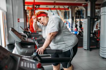 Overweight tired woman running on a treadmill in gym. Calories burning, obese female person in sport club