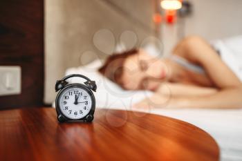 Alarm clock on the table, woman covering her ears with pillow, waking up. Morning bedding