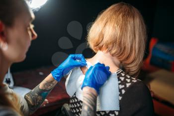 Female tattoo artist in blue sterile gloves prepares client skin for tattooing. Tattoo salon
