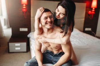 Happy love couple with naked body hugging on big white bed. Intimate games in bedroom, intimacy lovers