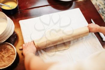 Male chef roll out the dough with a rolling pin, top view, wooden kitchen table on background. Homemade strudel cooking