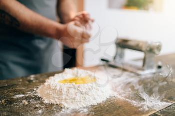 Homemade pasta cooking, male chef preparing dough. Egg and bunch of flour on wooden table