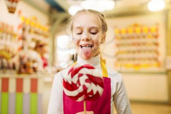 Happy little girl holds fresh lollipop in candy store. Handmade sugar caramel on stick