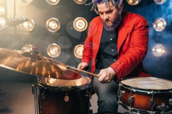 Bearded drummer in red suit, performing on the stage with lights, retro style. Musical performer with colorful hair, drum instrument