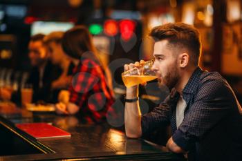 Young man drinks beer at the bar counter in a sport pub, happy leisure of football fan