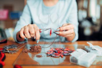Female person holds pliers, master at workplace. Handmade jewelry. Needlework, fashion bijouterie making