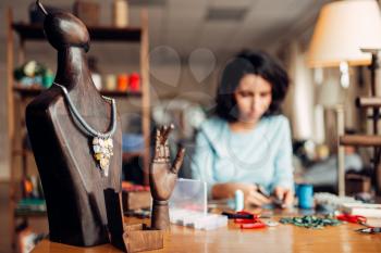 Handmade necklace on a wooden mannequin, needlework. Female craftman at the workplace on background