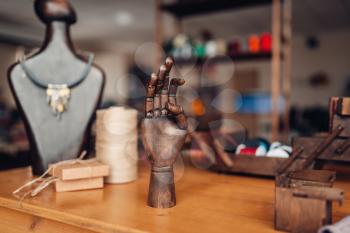 Needlework accessories, wooden hand and mannequin with handmade bijouterie on the table in workshop, closeup. Handmade jewelry