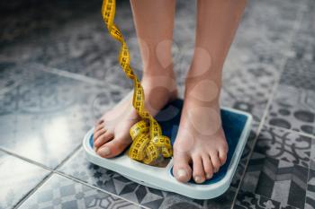 Female feet on the scales closeup, measuring tape. Fat or calories burning concept. Weight loss, hard dieting