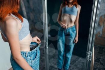 Thin woman tries on big size jeans against mirror, weight loss, anorexia. Fat or calories burning concept, medical illness 