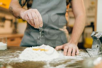 Homemade pasta cooking, man preparing dough. Egg and bunch of flour on wooden table