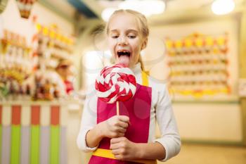 Happy little girl holds fresh lollipop in candy store. Handmade sugar caramel on stick
