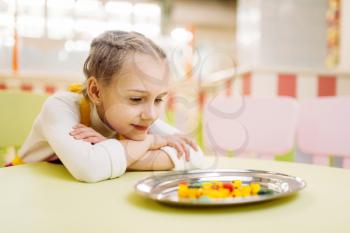 Little girl watching on handmade sugar caramel in plate, development of willpower. Fresh lollipop in candy store