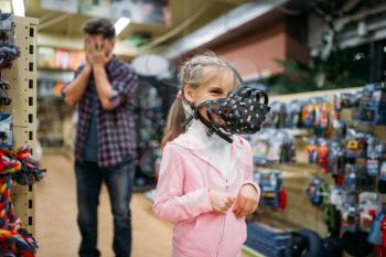 Father and little daughter having fun in petshop. Family chooses muzzle for dog in pet shop