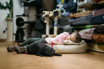 Little girl with puppy are sleep in pet shop. Kid with dog in petshop, goods for domestic animals