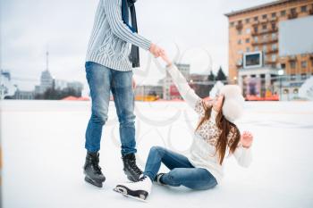 Male person helps a woman to get up, love couple on skating rink. Winter ice-skating on open air, active leisure
