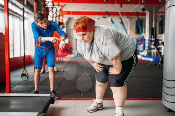 Instructor forces fat woman to exercise, hard workout in gym. Calories burning, obese female person in sport club, fat-burning motivation