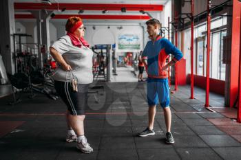 Fat woman talks with instructor after exercise with rope in gym. Calories burning, obese female person on hard training in sport club