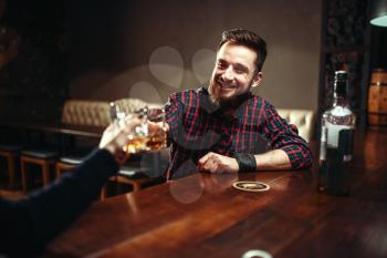 Two men clink glasses at a bar, friends drink strong alcohol and having fun. Happy leisure in pub