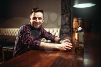Smiling man sitting at the bar counter, relaxation with alcohol. Happy guy having fun in pub