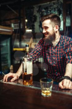One man with bottle of alcohol beverage in hand standing at the bar counter. Male person in pub, alcoholism, drunkenness