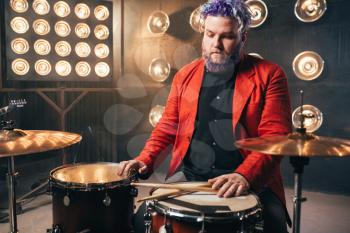 Bearded drummer in red suit, performing on the stage with lights, vintage style. Musical performer with colorful hair, drum instrument