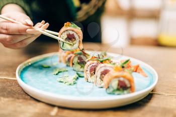 Male person eats sushi rolls with chopsticks, japanese kitchen. Traditional asian food, seafood delicious